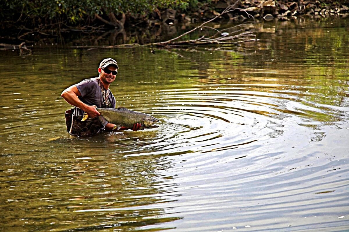 Smiling fisherman gently holding a fish in river during catch and release fishing